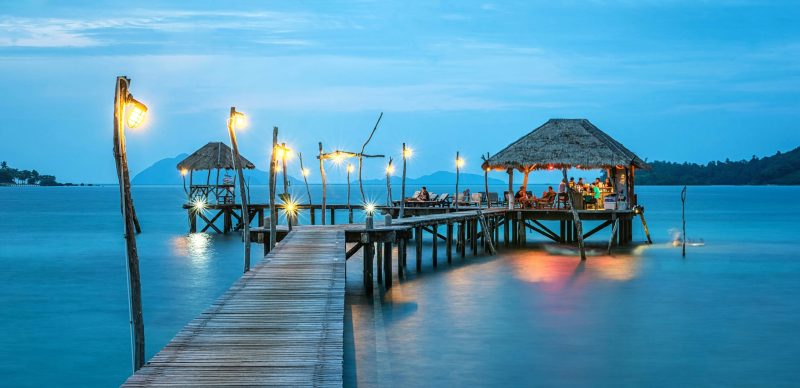 Illuminated pier and bungalow on a tranquil tropical sea at twilight.