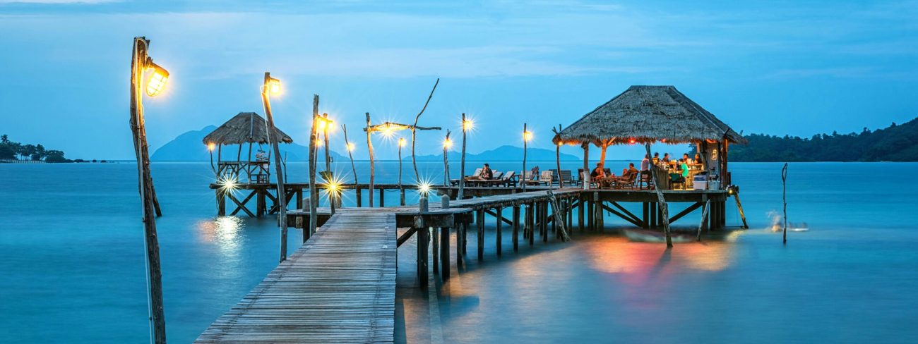 Illuminated pier and bungalow on a tranquil tropical sea at twilight.